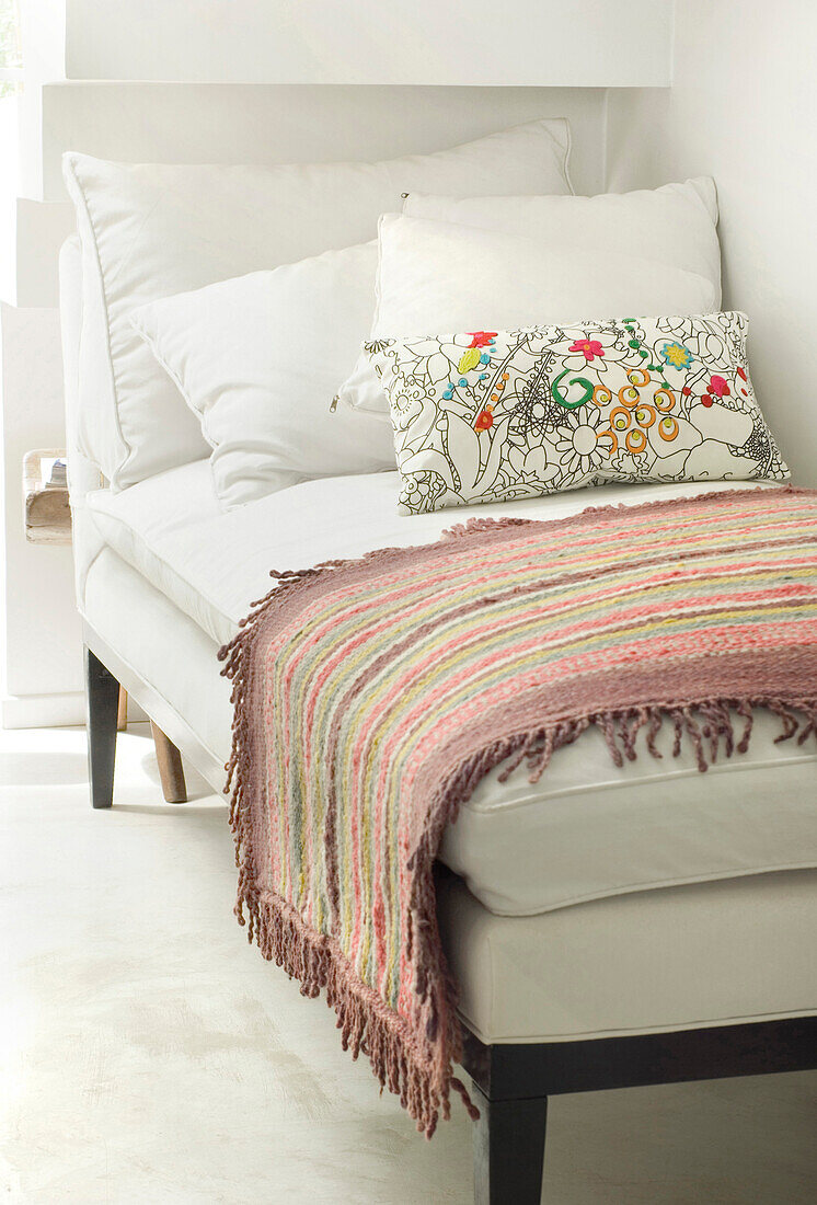 Weißes Tagesbett mit Blumenkissen und gestreiftem Teppich