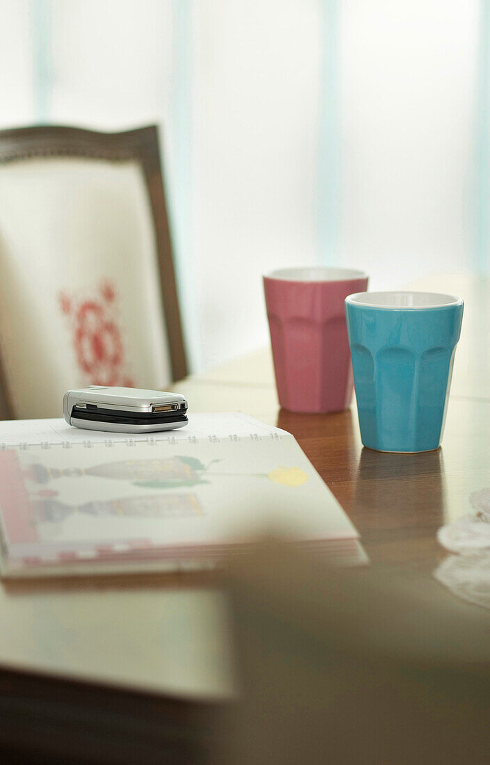 Mobile phone on open book on dining table with ceramic cups