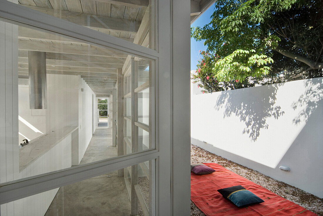 Bodenkissen auf einem Teppich und Blick durch ein Fenster auf den Korridor eines Strandhauses aus Beton
