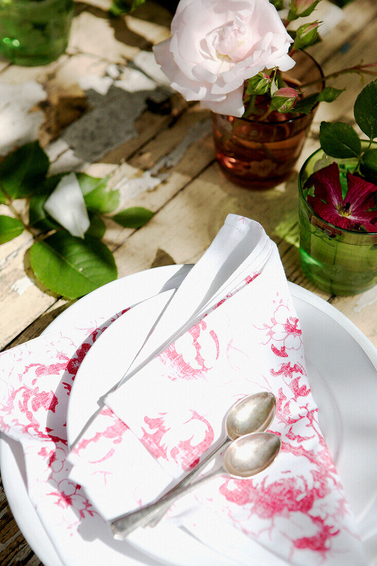 Serviette und Teelöffel auf Teller auf Holztisch mit rosa Rose