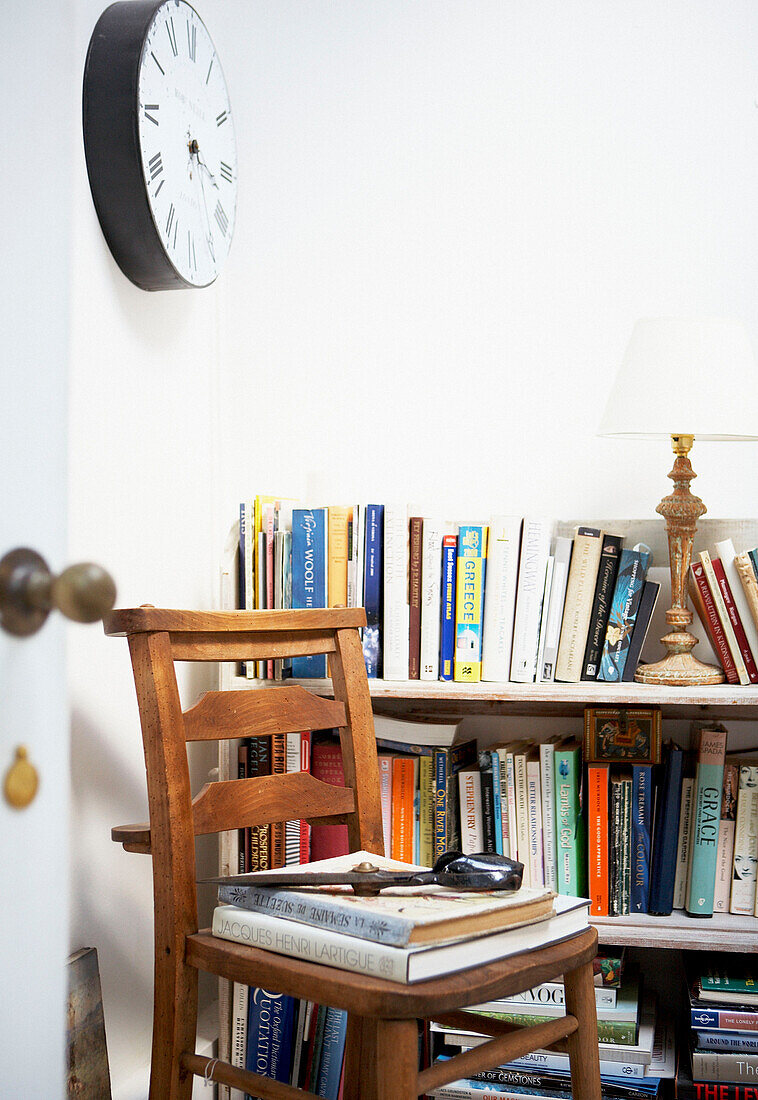 Holzstuhl unter Uhr mit Bücherregal