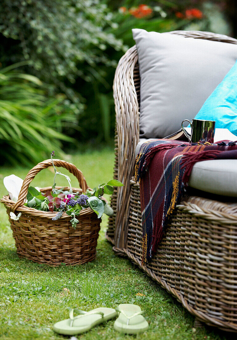 Cane daybed and basket of cut flowers on garden lawn