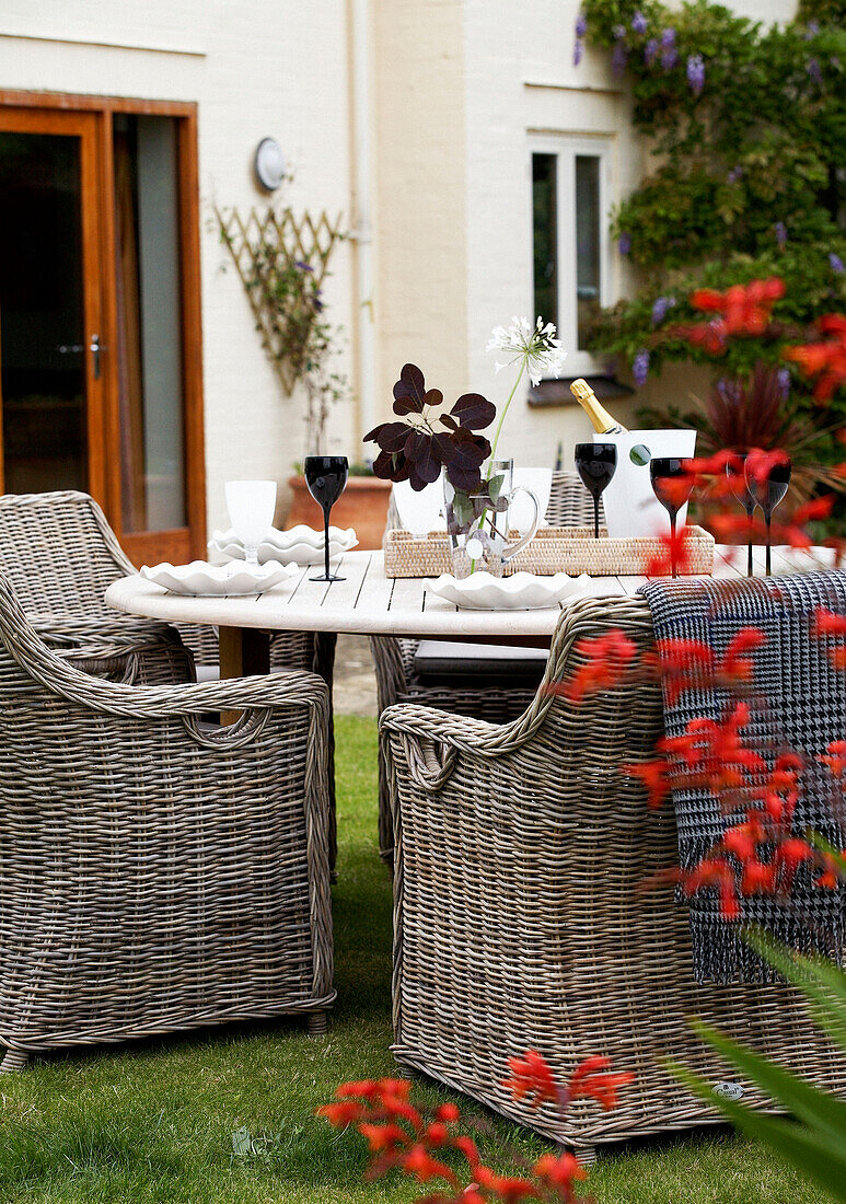 Cane furniture at garden table with wineglasses and ice bucket