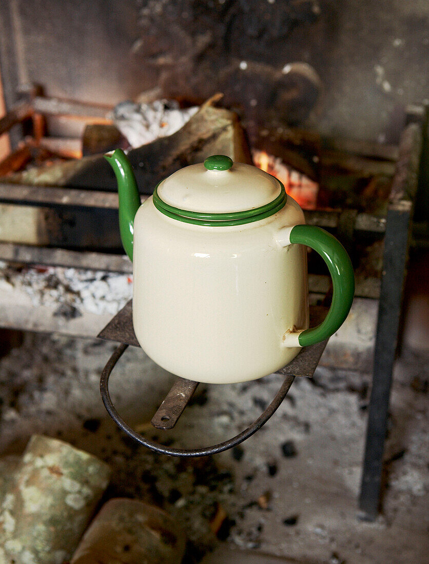 Cream teapot with green trim on fireplace stove