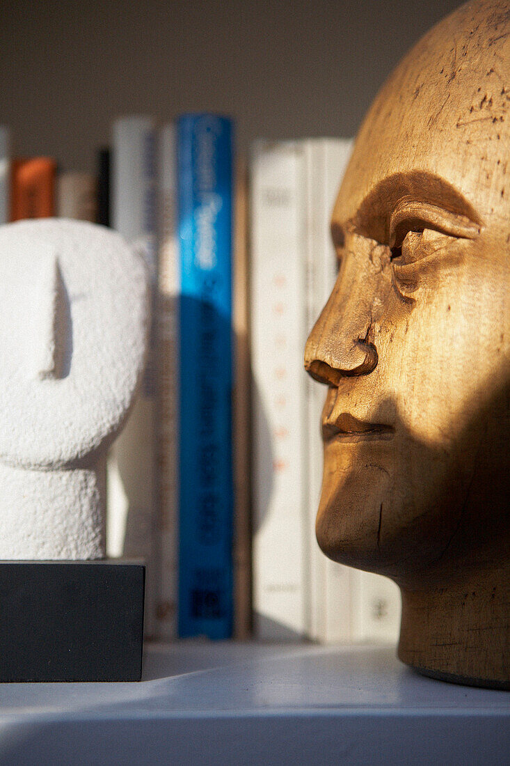 Aus Holz geschnitzter skulpturaler Kopf auf Bücherregal
