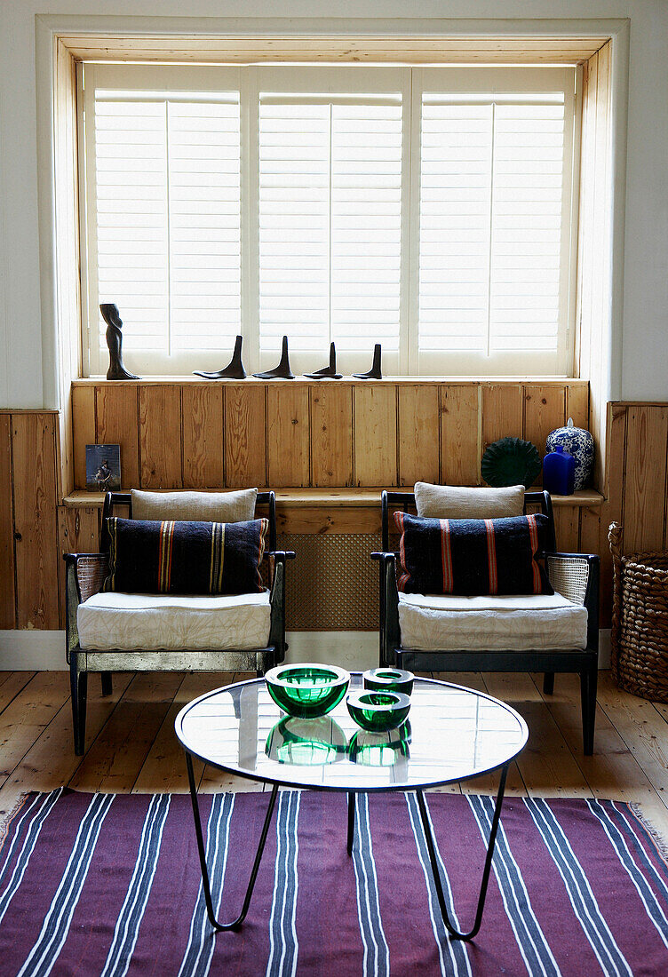 Passende Stühle unter einem sonnendurchfluteten Fenster mit einem Couchtisch mit Glasplatte auf einem gestreiften Bodenteppich