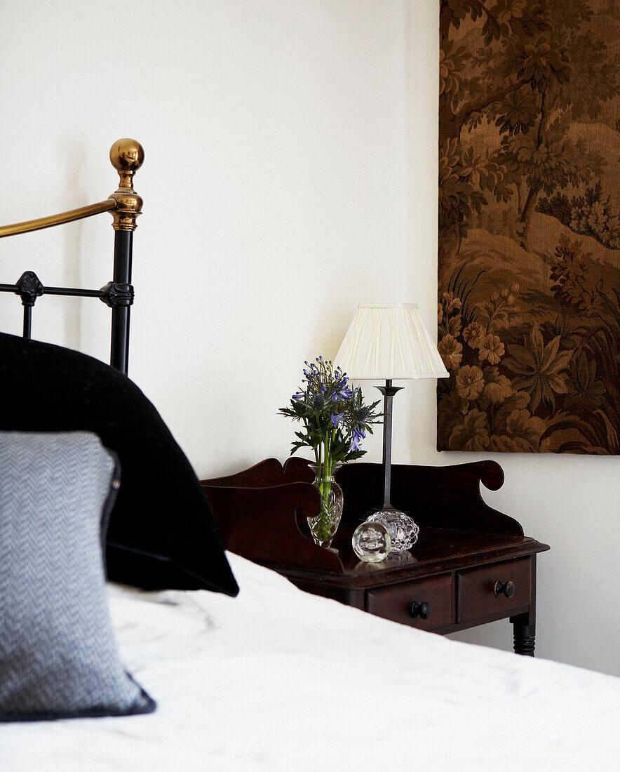 Bettkopfteil aus Messing mit antikem Nachttisch aus dunklem Holz und Wandbehang aus Gobelin