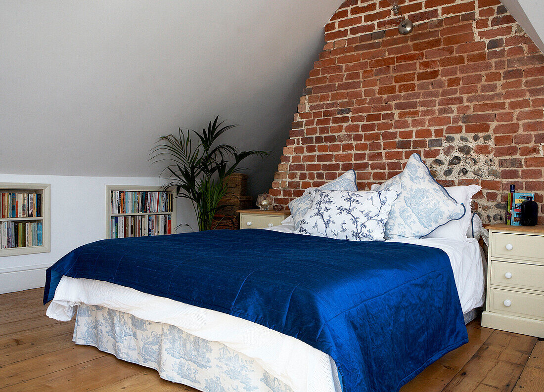 Vibrant blue bed cover in attic room with exposed brick chimney flue