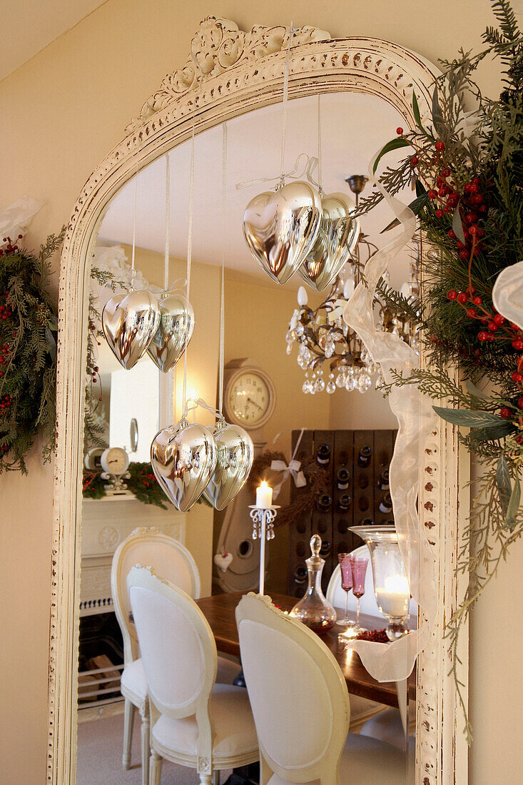 Weihnachtskränze und silberne herzförmige Dekorationen hängen an einem bemalten Spiegelrahmen
