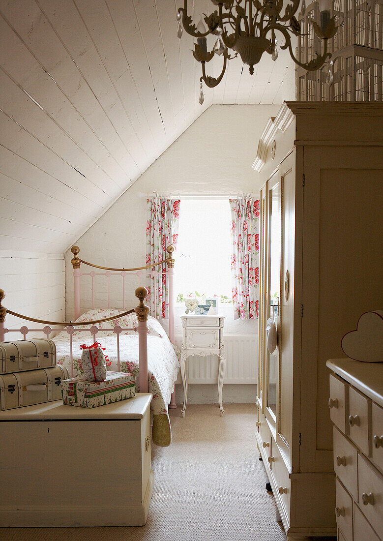 Weiß gestrichenes Schlafzimmer mit geblümten Vorhängen und Messingbett