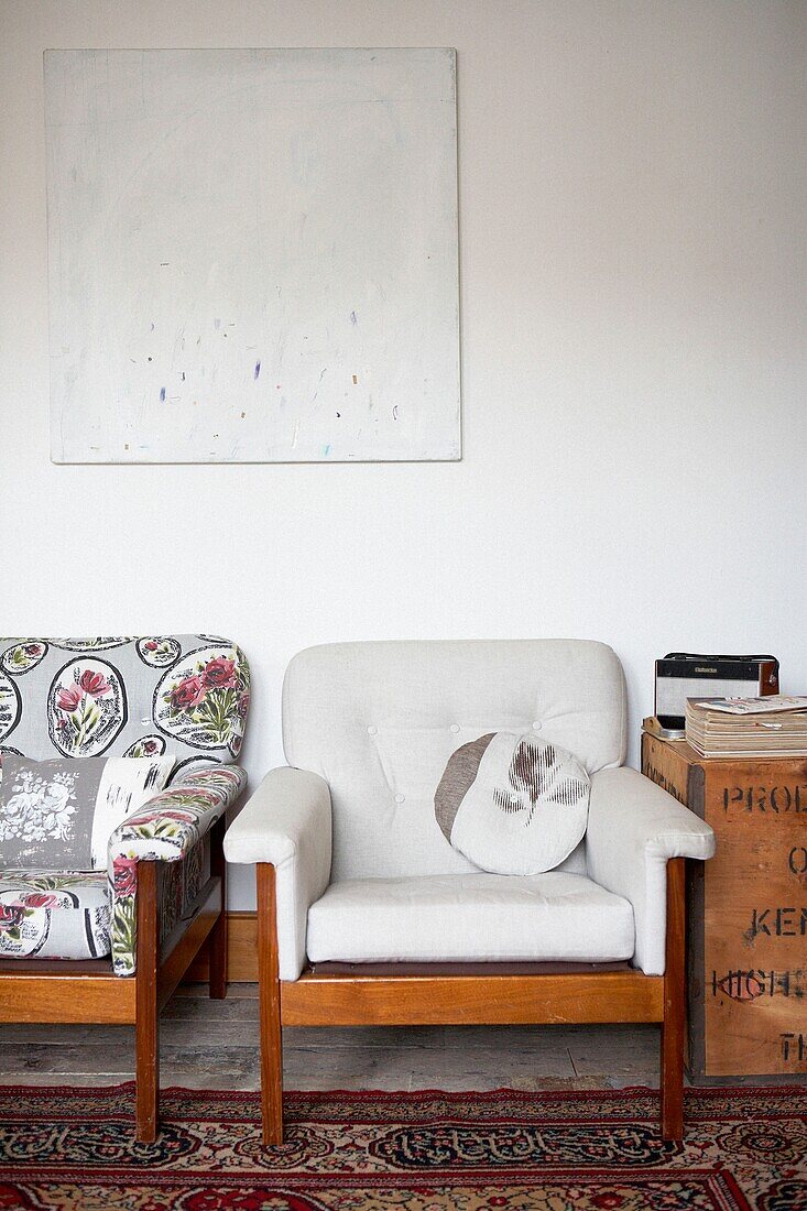 Mismatched armchairs below artwork with tea chest