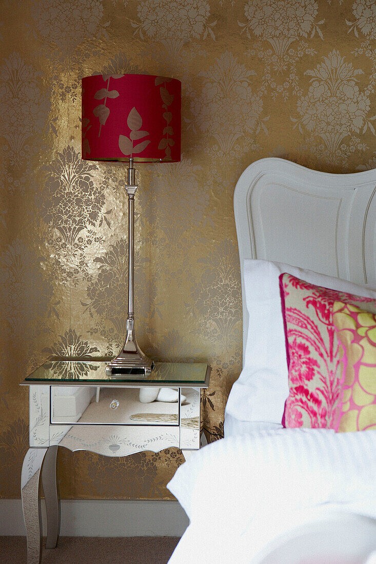Elegant bedside detail with gold wallpaper and mirrored bedside furniture