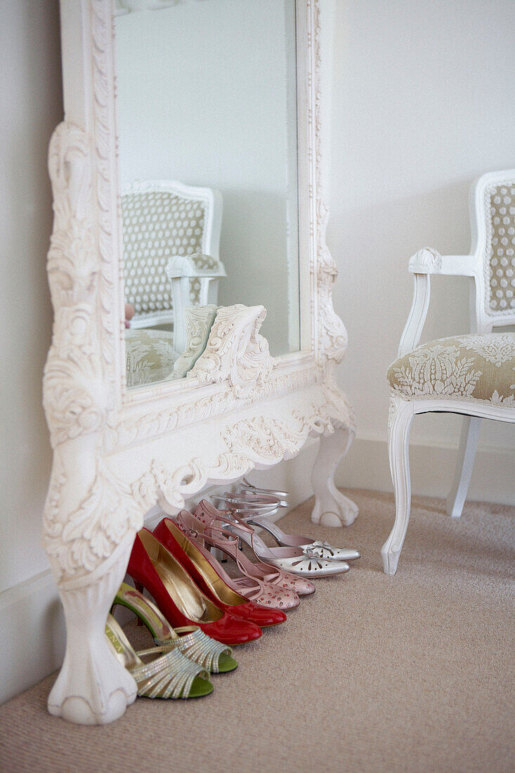 Detail eines Ankleidezimmers mit Damenstöckelschuhen in einer Reihe unter einem verzierten geschnitzten Spiegel und einem Stuhl