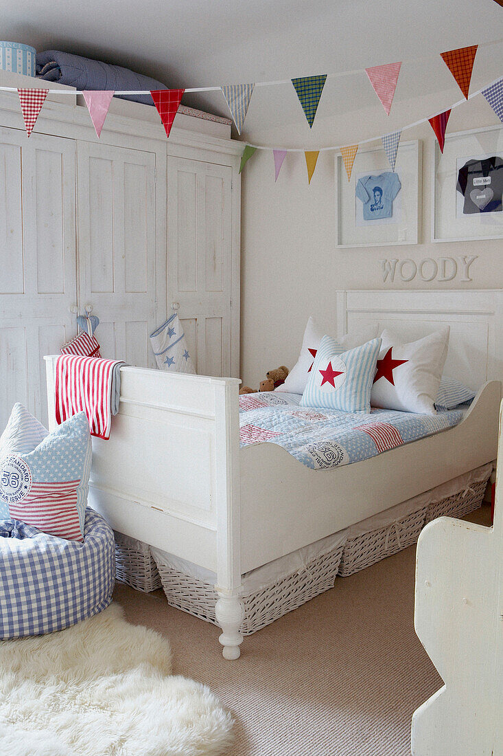 Childs bedroom with bunting and star cushions with painted white furniture and framed baby clothes