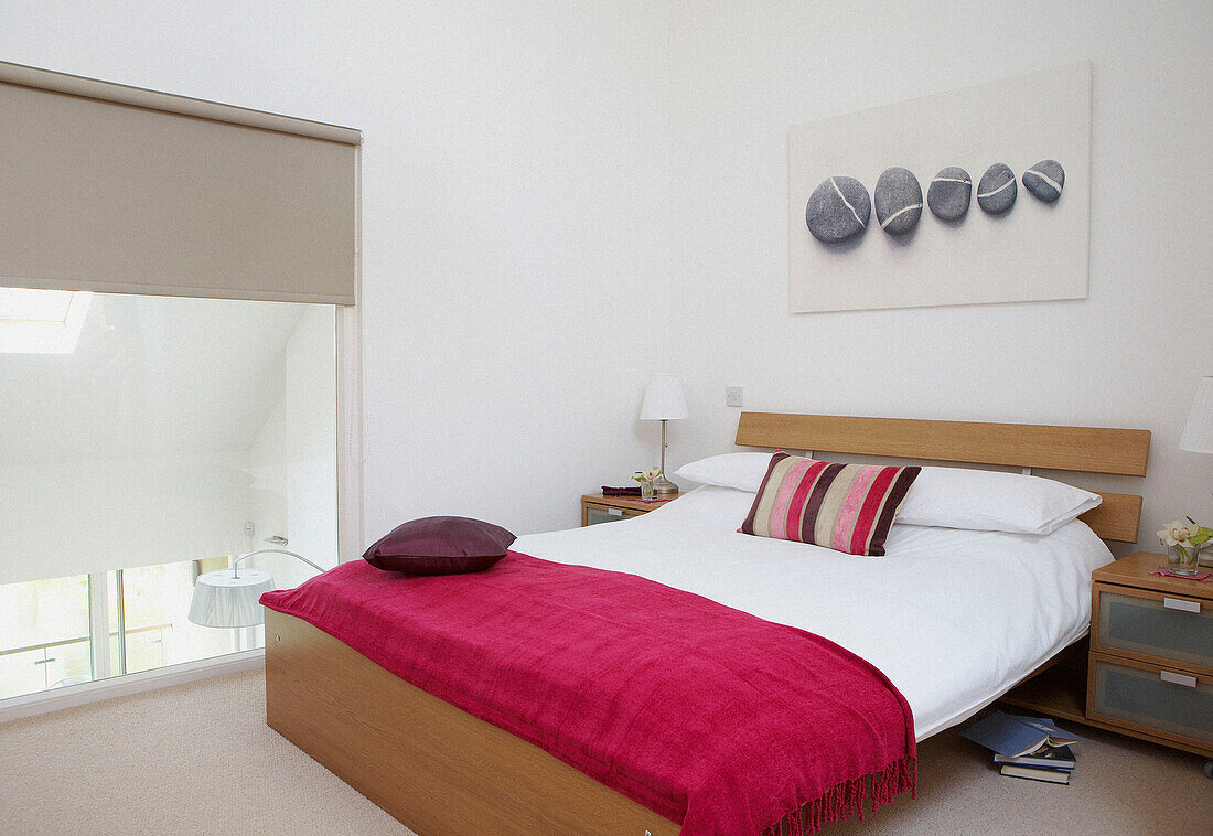 Pink blanket on double bed of eco house with large glazed windows which allow the sun to heat the building