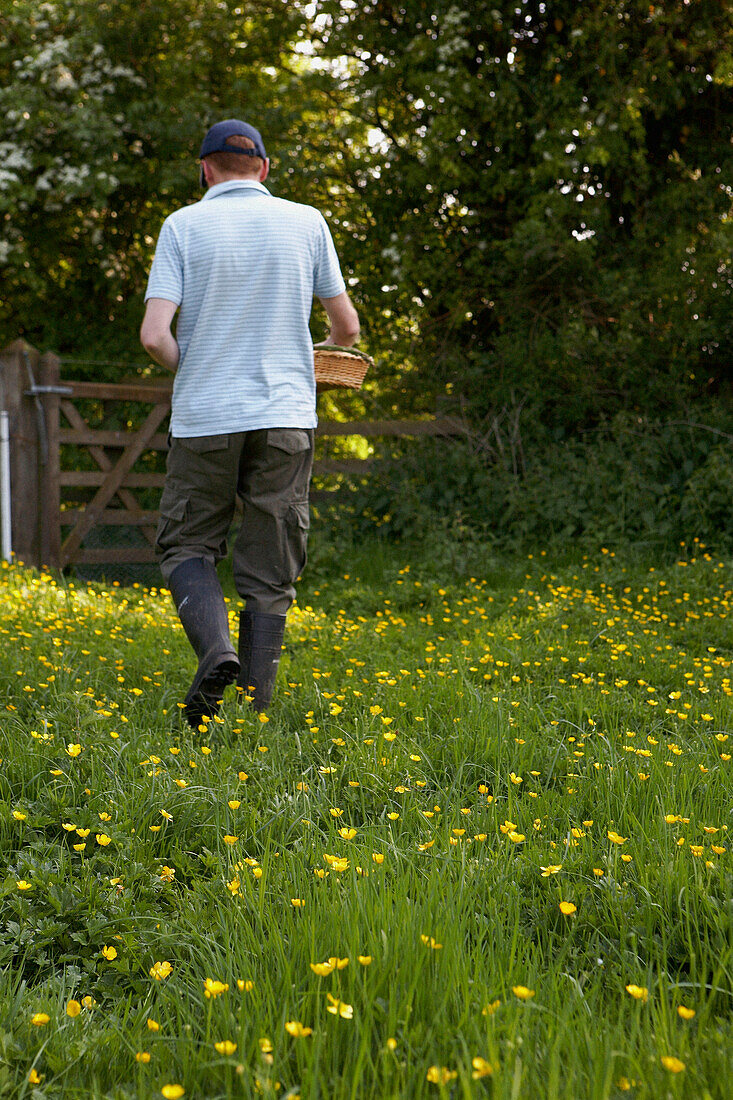 Man walks towards gate in Gloucestershire meadow carrying basket