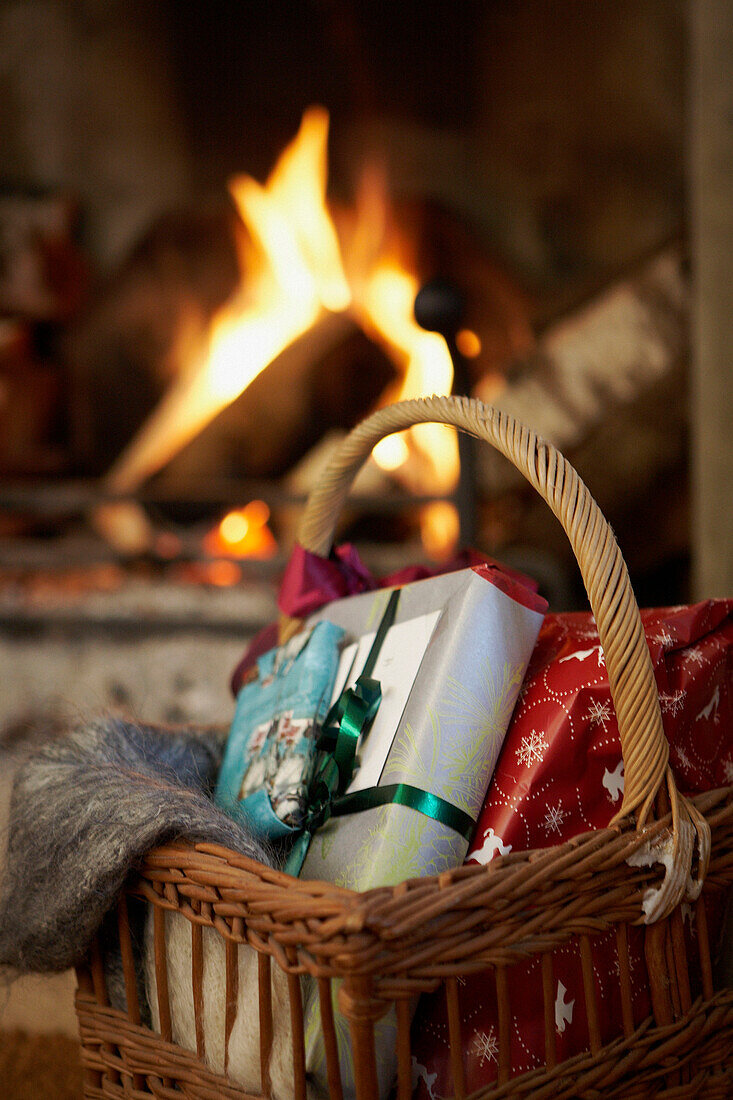 Weihnachtsgeschenke in einem Korb neben dem offenen Kamin