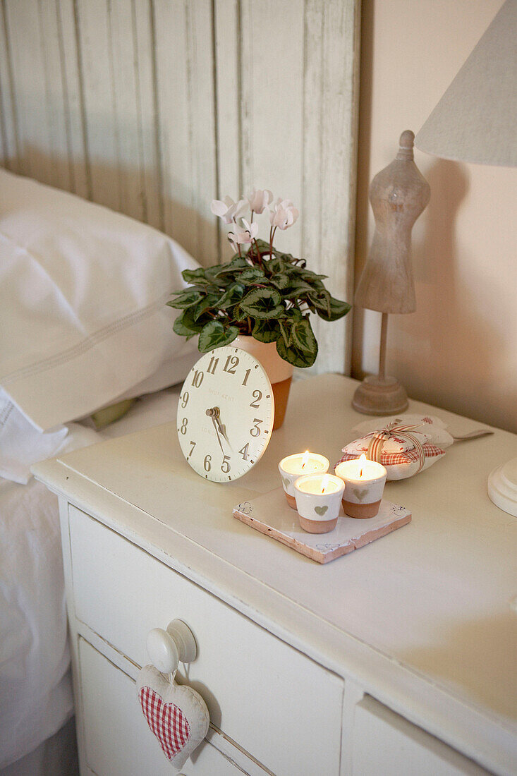 Uhr und brennende Kerzen mit Zimmerpflanze auf dem Nachttisch