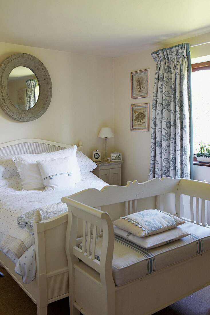 Double bed with white painted bench and blue floral patterned curtains