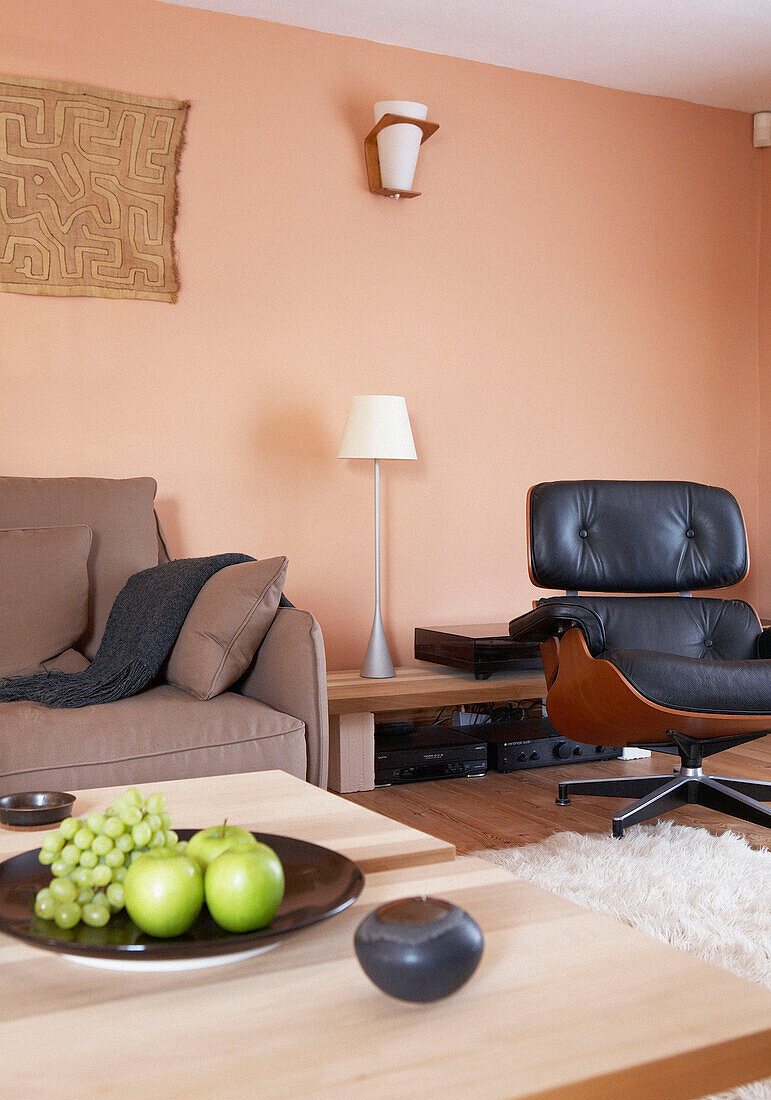 Black leather Charles Eames chair in peach coloured living room with fruit bowl on table