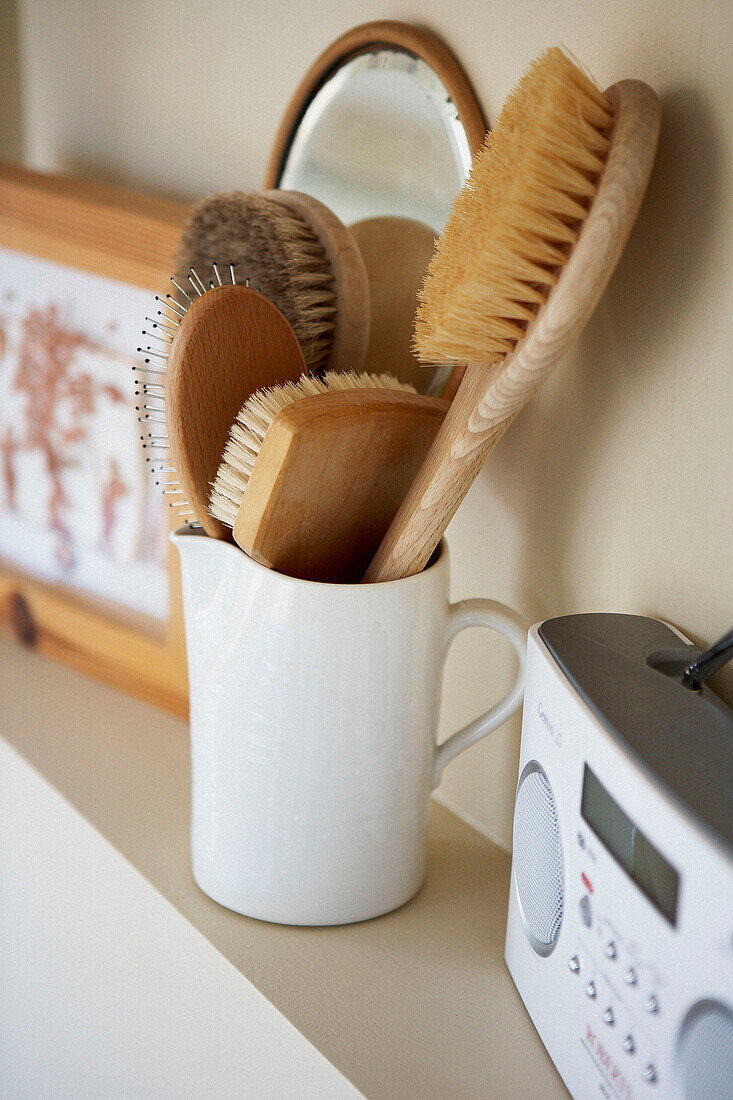 Selection of hairbrushes in jug on bathroom shelf