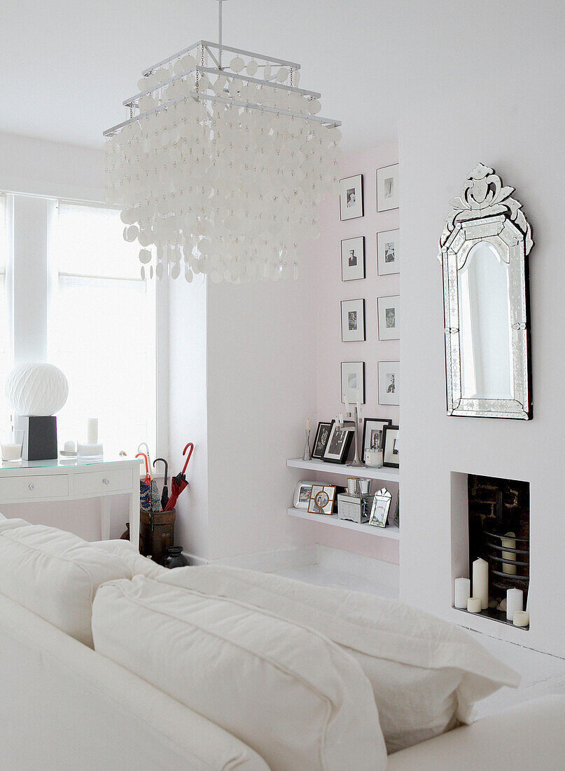 Ganz in Weiß gehaltenes Wohnzimmer mit dekorativen Lampenschirmen, Kunstwerken und Spiegeln mit Silberprägung