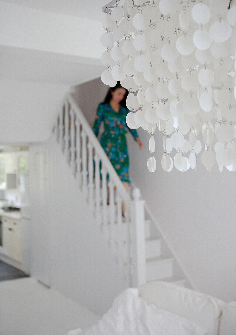 Frau geht die Treppe eines ganz in Weiß gehaltenen Hauses mit dekorativen Beleuchtungskörpern hinunter
