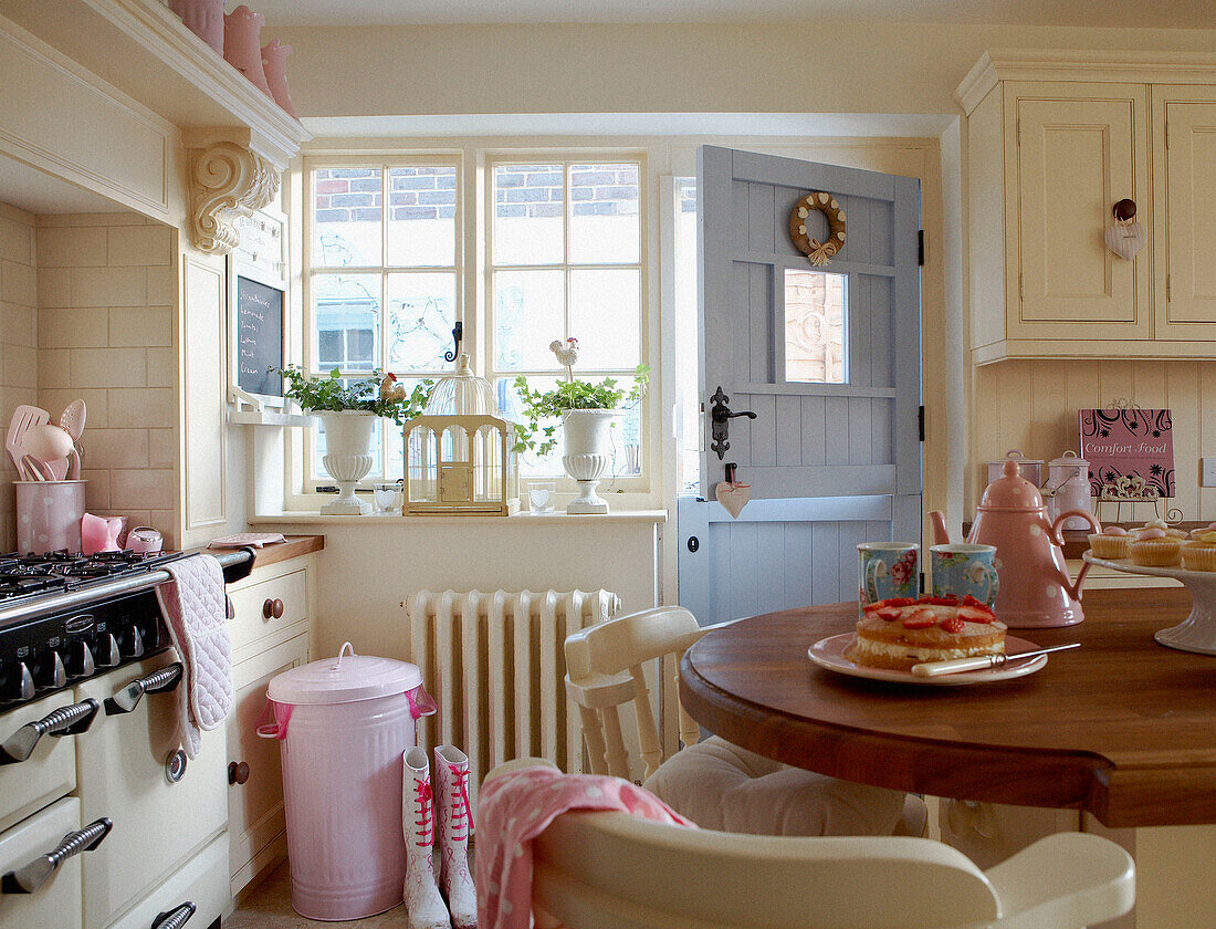 Cremefarbene, sonnenbeschienene Landhausküche mit rosa Accessoires und pastellblauer Hintertür