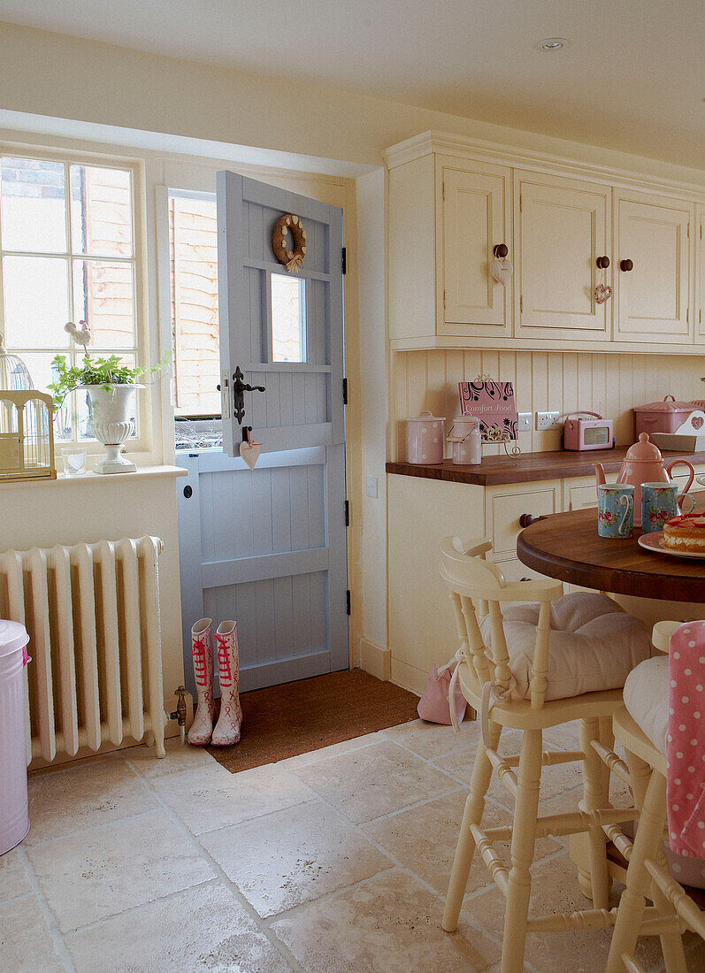 Cremefarbene, sonnenbeschienene Landhausküche mit rosa Accessoires und pastellblauer Hintertür
