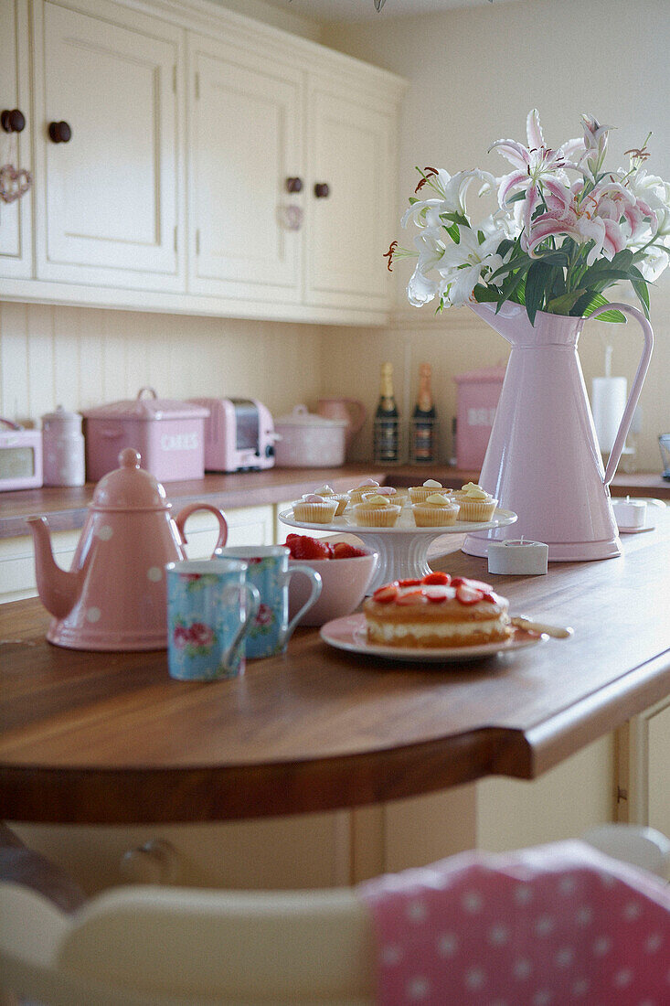 Pink tableware and cream cakes on wooden worktop 