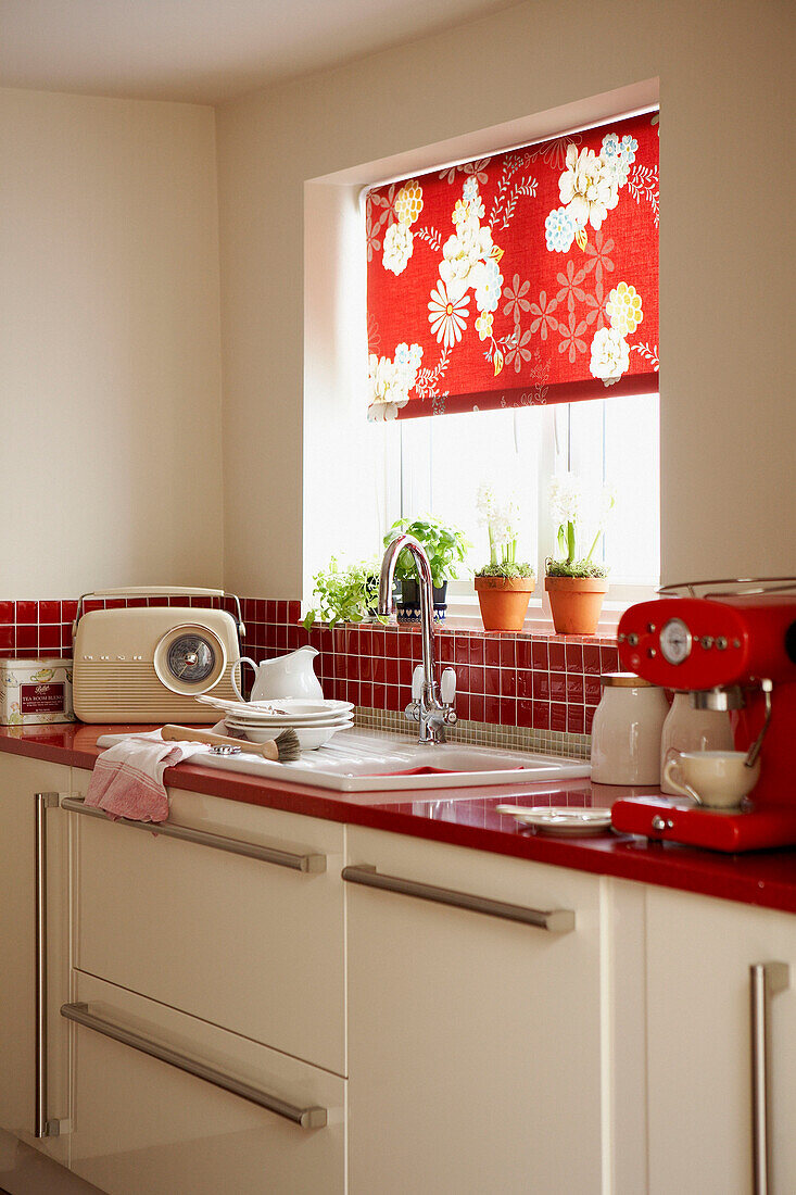 Red tiled kitchen with washing up and floral patterned roller blind