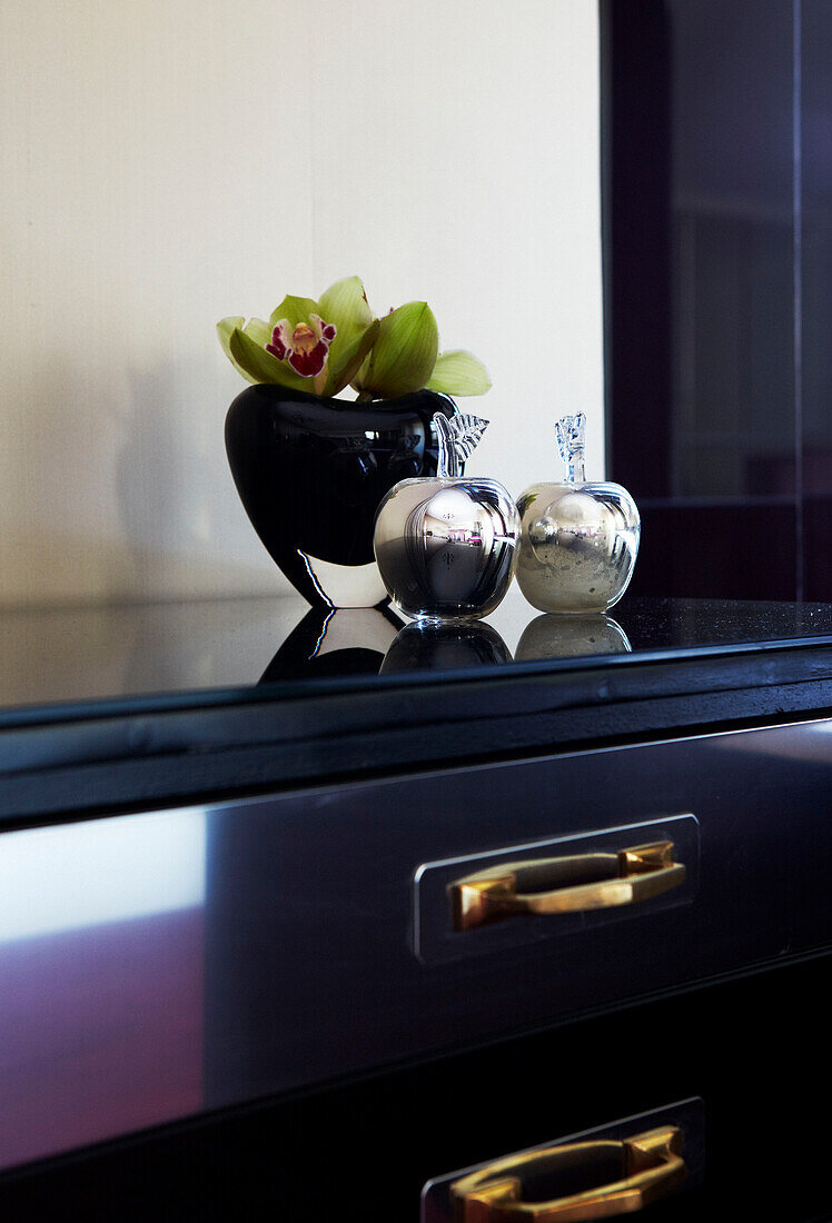 Metallornamente in Form eines Apfels und eine Blumenvase auf einer Tischplatte mit Schublade
