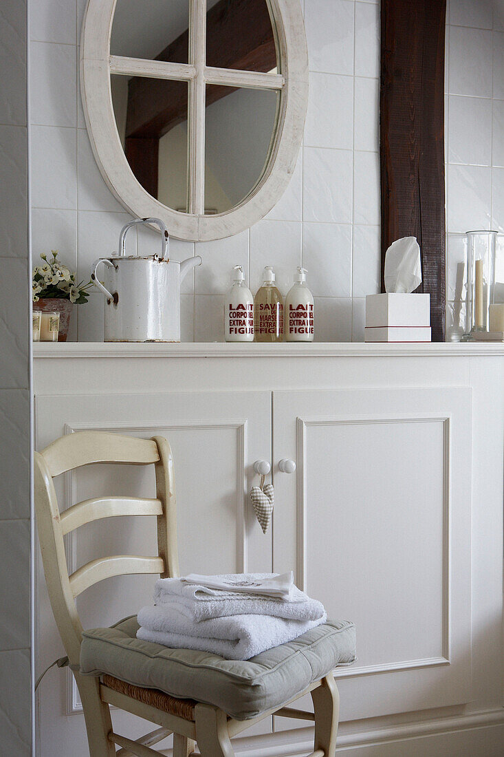 Cream painted chair and built in cupboards with oval shaped bathroom mirror 