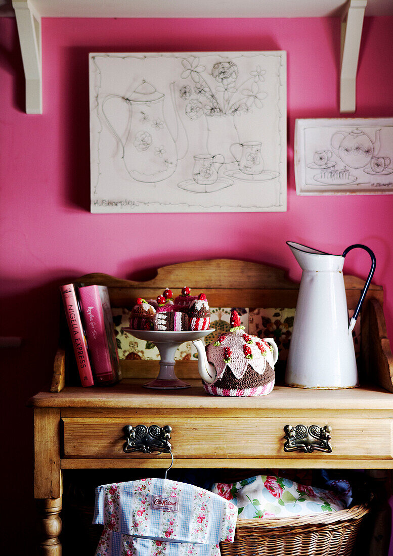 Knitted teacakes and teacosy on sideboard in pink room with artwork