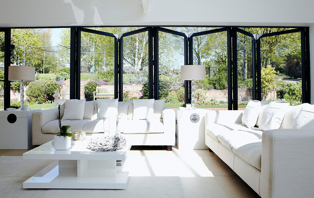 Wohnzimmer mit weißem Sofa und Faltenbalgtüren, die zum Garten führen