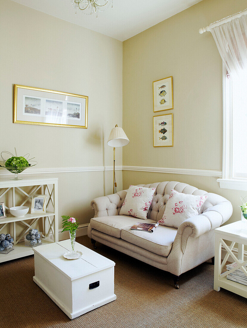 Blumenkissen auf cremefarbenem Sofa mit weiß gestrichenem Kasten und Regalen