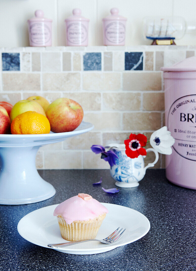 Teekuchen auf der Theke mit Obstschale und rosa Küchenutensilien