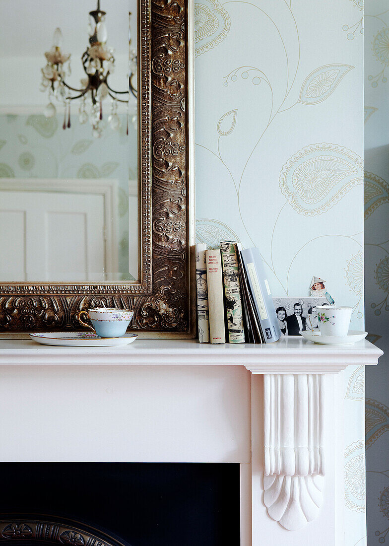 Books and teacups on mantlepiece with gilt framed mirror