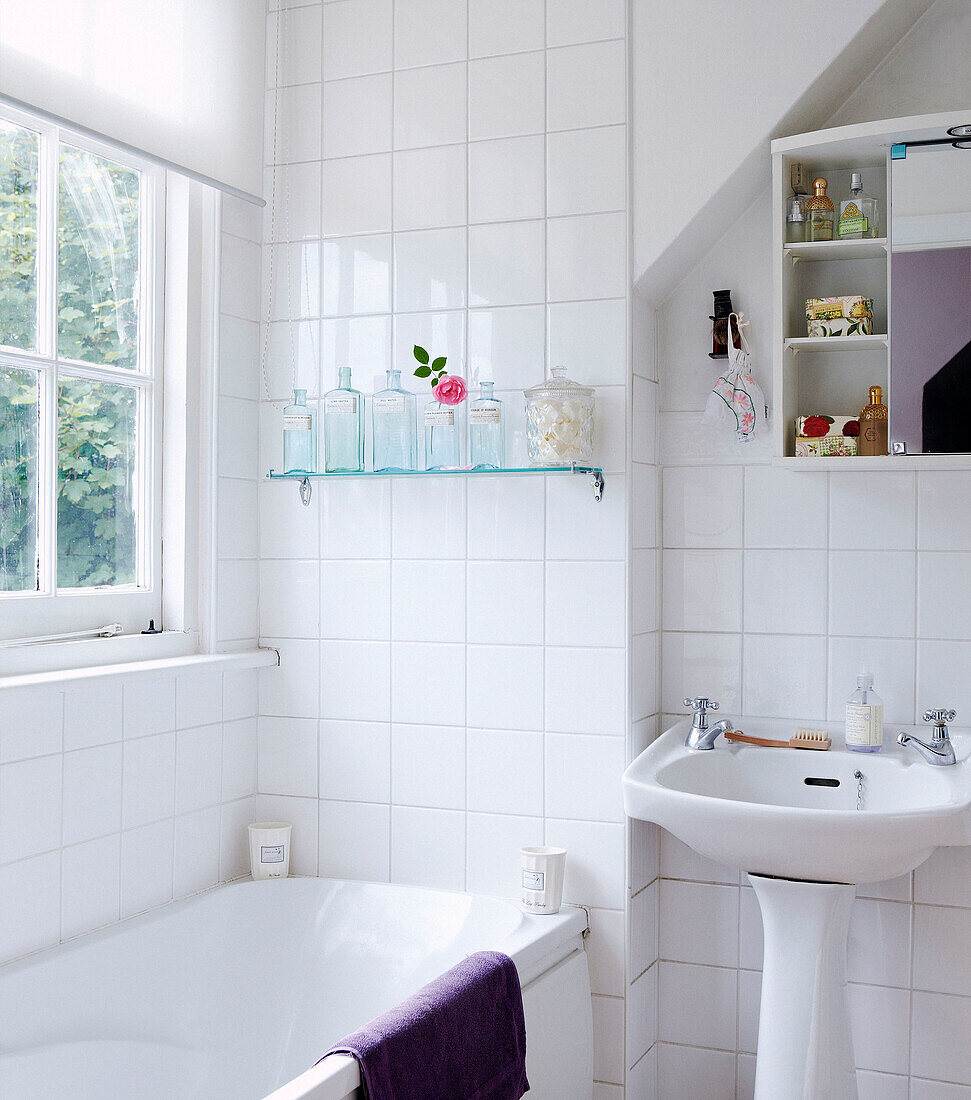 Tiled white bathroom with cabinet storage and glass shelf