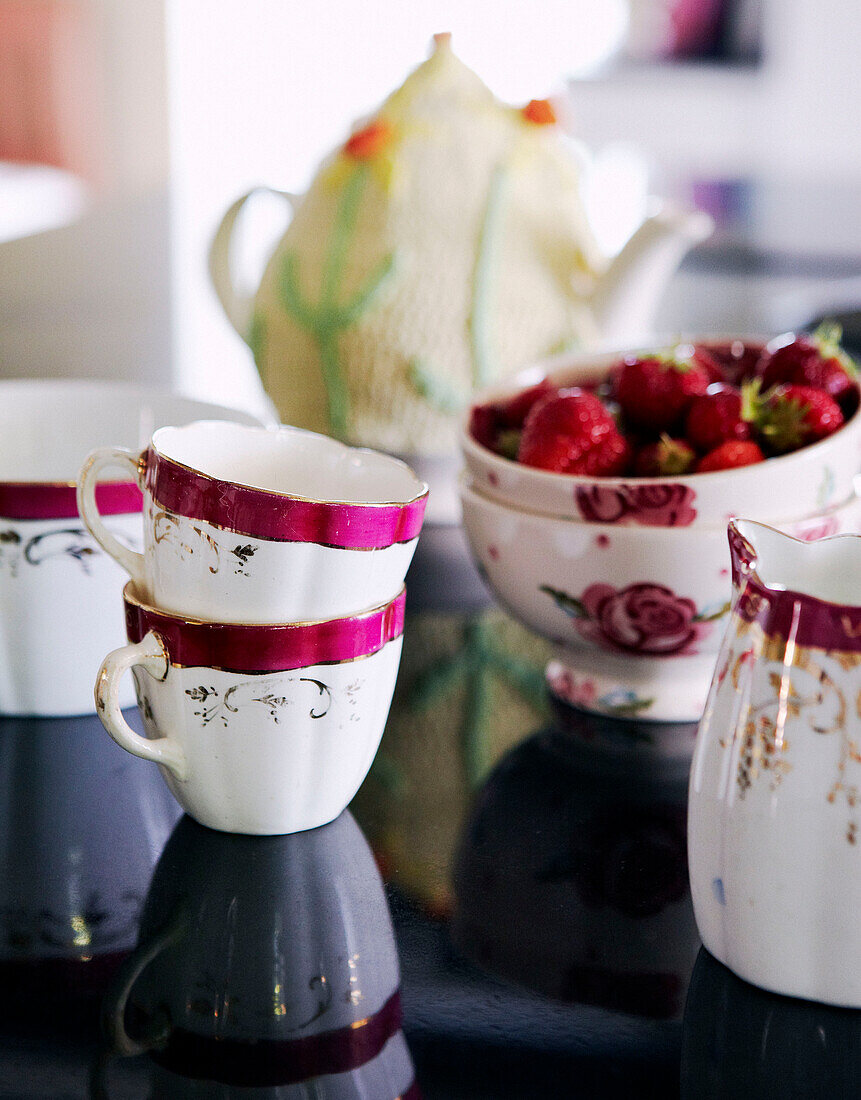 Hübsche rosa und weiße Porzellantassen und -schalen mit Erdbeeren auf einem Tisch