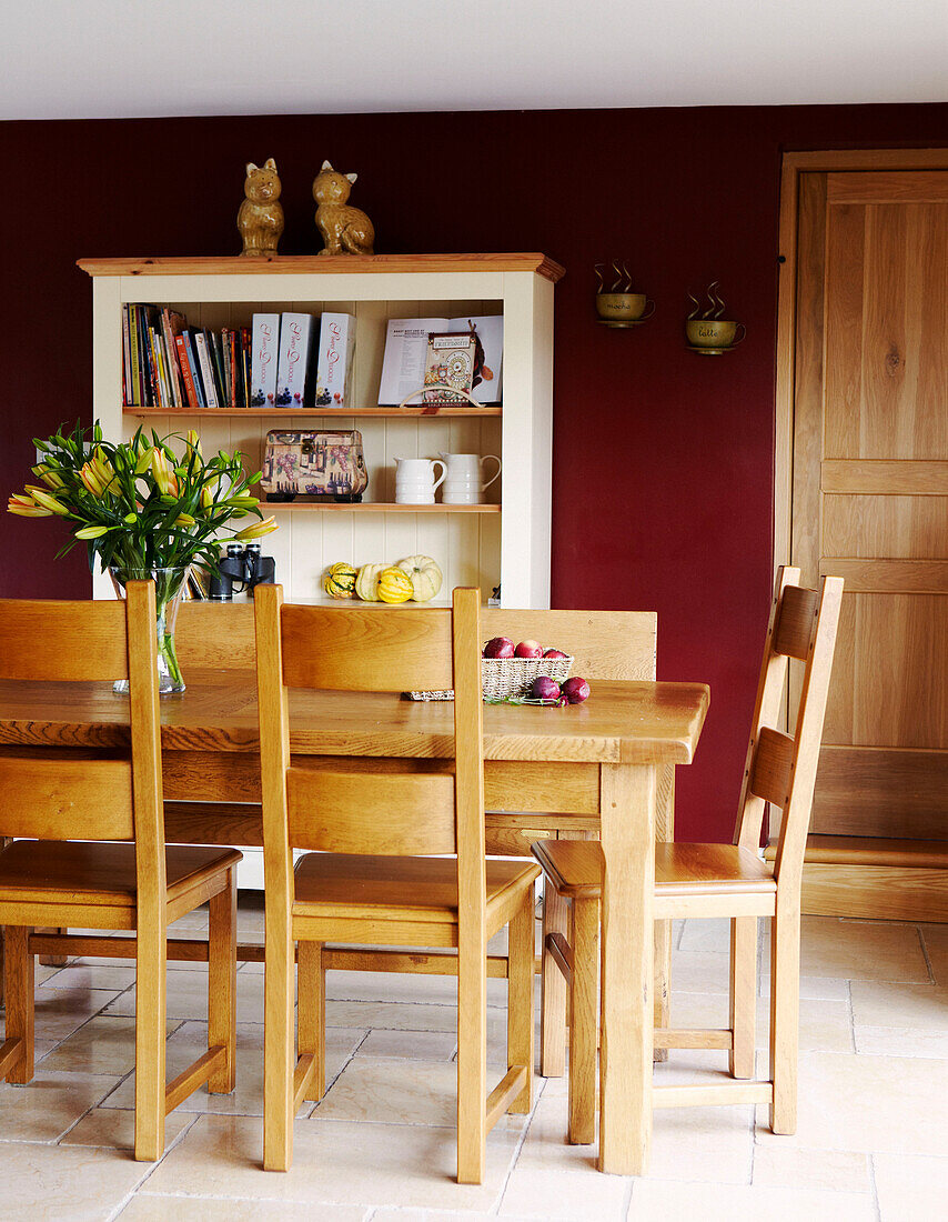 Dining room table and chairs with dark red walls and bookcase