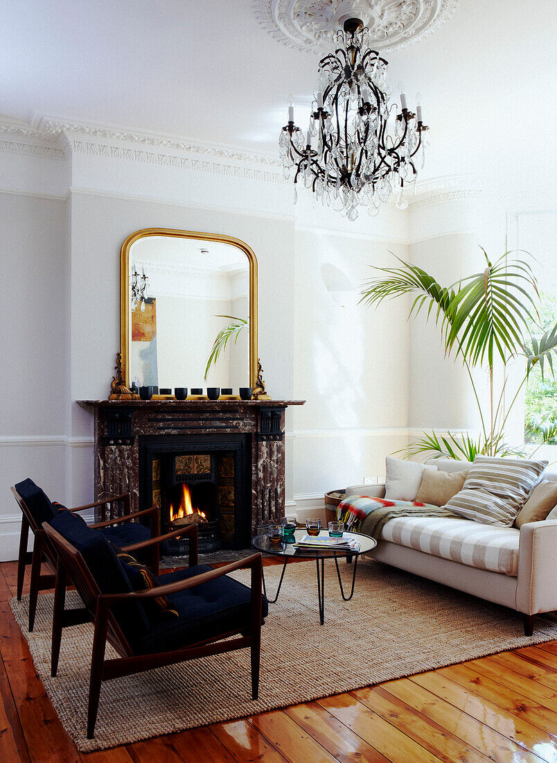 Lit fire in living room with matching armchairs and glass chandelier
