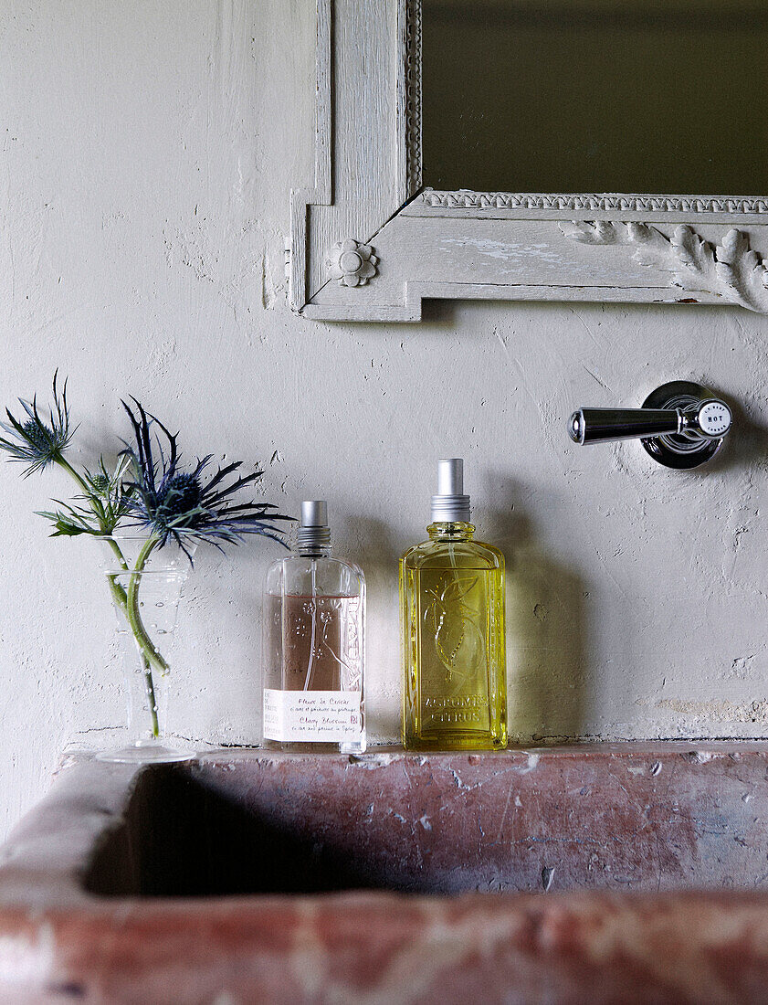 Toilettenartikelflaschen und Schnittblumen auf einem Marmorbecken in einem Landhaus