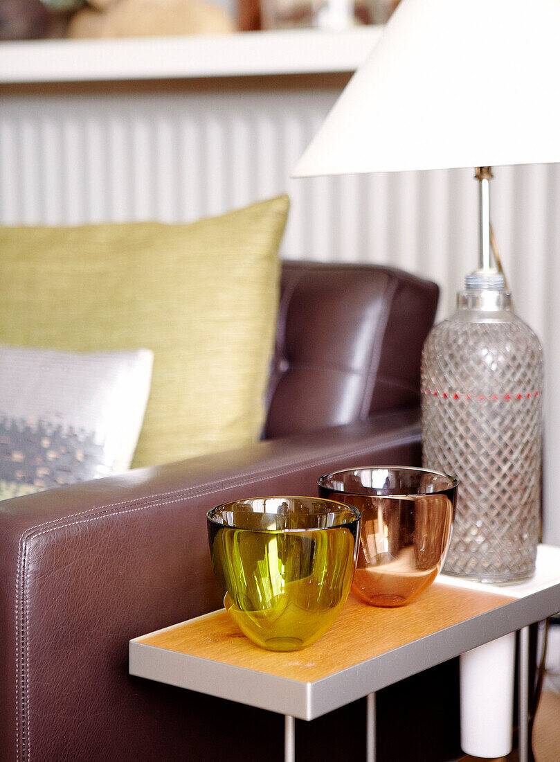 Lamp with soda bottle base and tea light holders on side table beside leather sofa