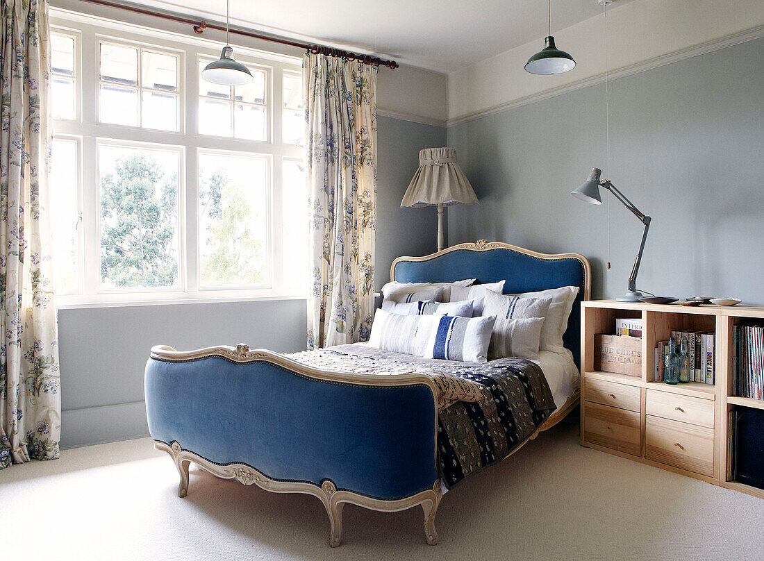 Blue and head and footboards on bed at window with wooden bedside storage unit