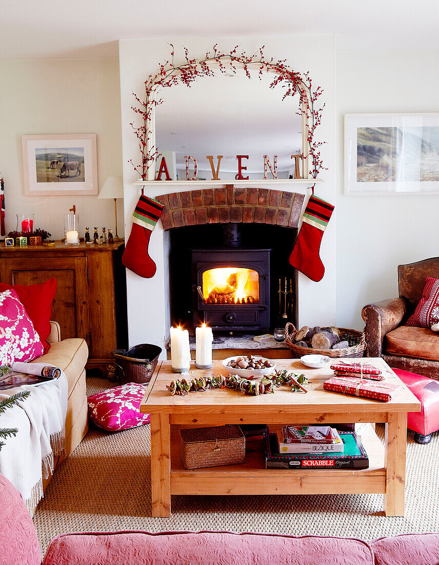 Christmas presents on wooden table in living room with stockings hanging on wood burning stove