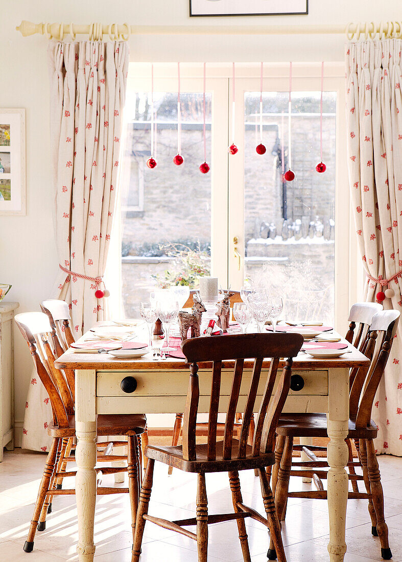Holzstühle an einem Tisch im Esszimmer mit Weihnachtskugeln im Türrahmen