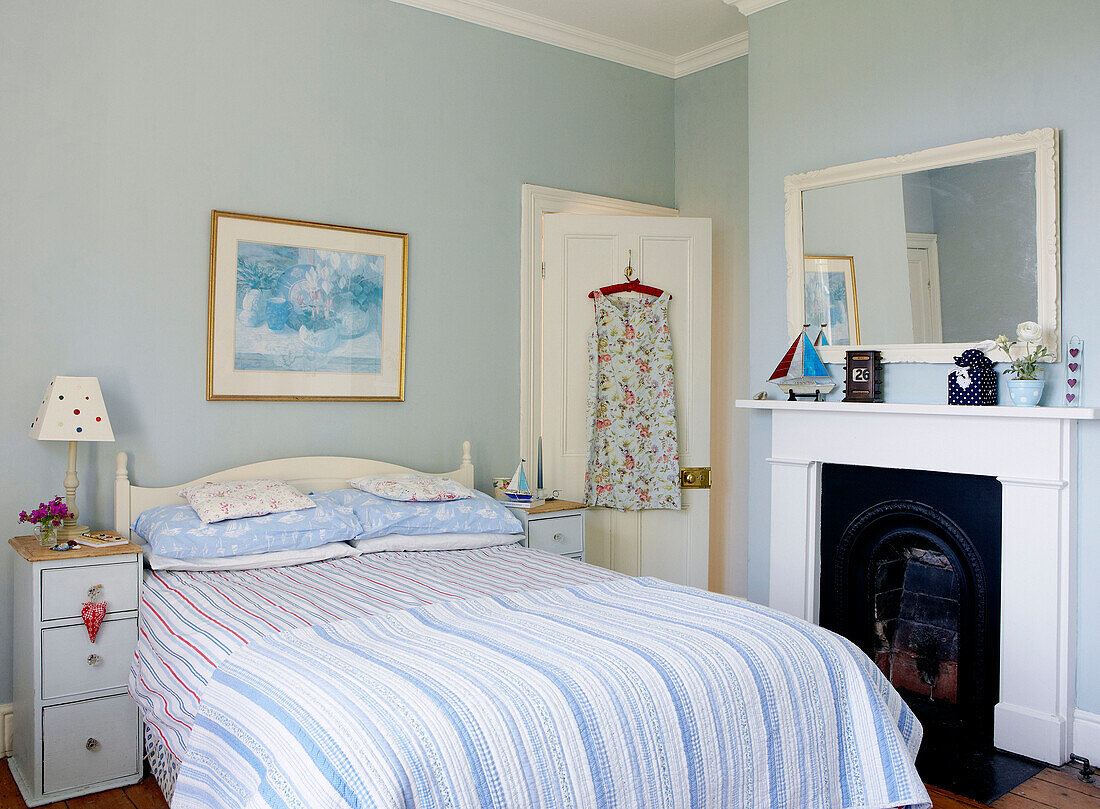 Sommerkleid hängt an der Rückseite der Tür in einem frischen blauen Schlafzimmer mit originalem Kamin