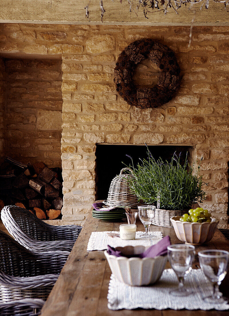 Geschirr und Korbstühle am Tisch im Außenbereich eines Landhauses aus Stein