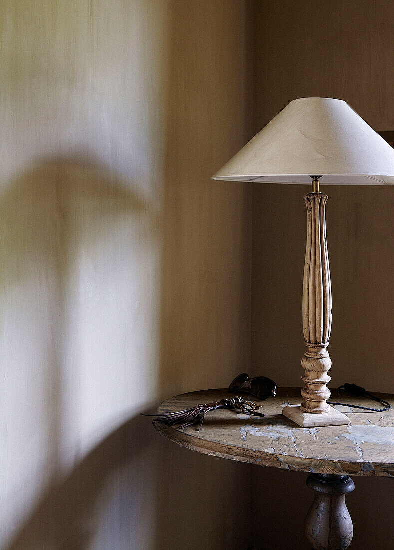 Cremefarbene Lampe mit geschnitztem Sockel auf einem Beistelltisch in einem Landhaus